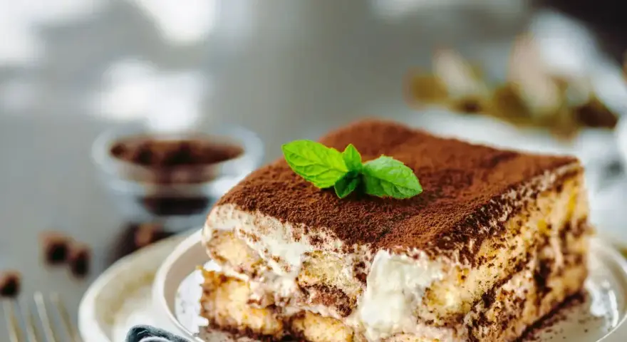 Una fetta di tiramisù ricetta originale, cosparso di cacao e decorato con menta fresca.