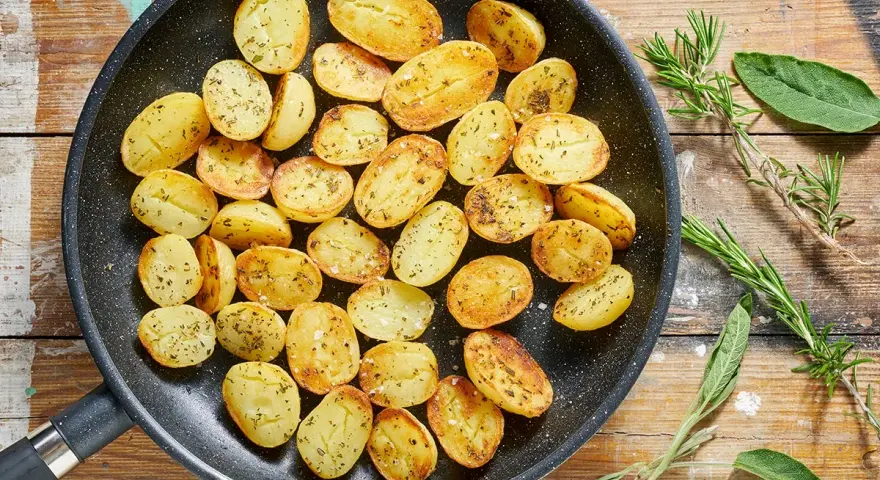 Patate novelle dorate e profumate in padella, condite con erbe aromatiche fresche, pronte per essere gustate.