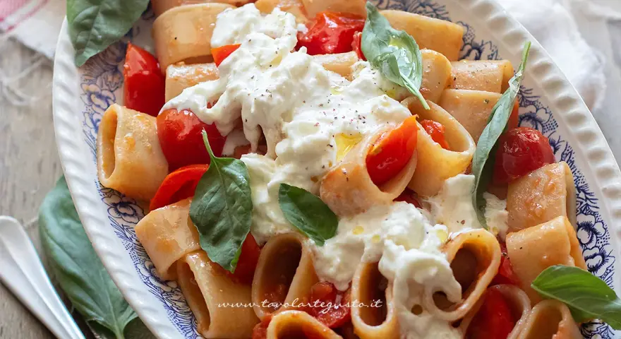 Piatto di pasta con pomodorini e abbondante stracciatella cremosa, guarnito con basilico fresco.