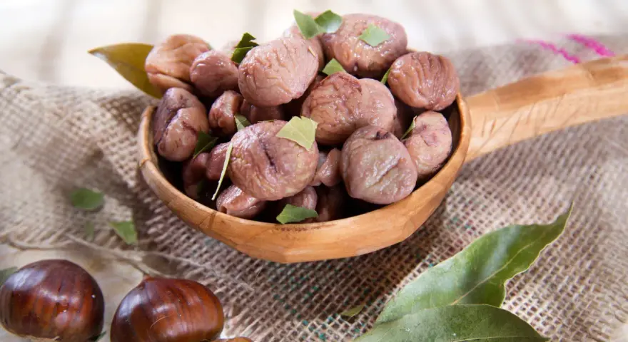 Un cucchiaio di legno trabocca di castagne bollite con buccia, guarnite con foglie verdi. Un assaggio autunnale.