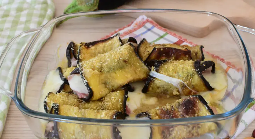 Involtini di melanzane alla siciliana appena sfornati, filanti e dorati, in una pirofila di vetro.