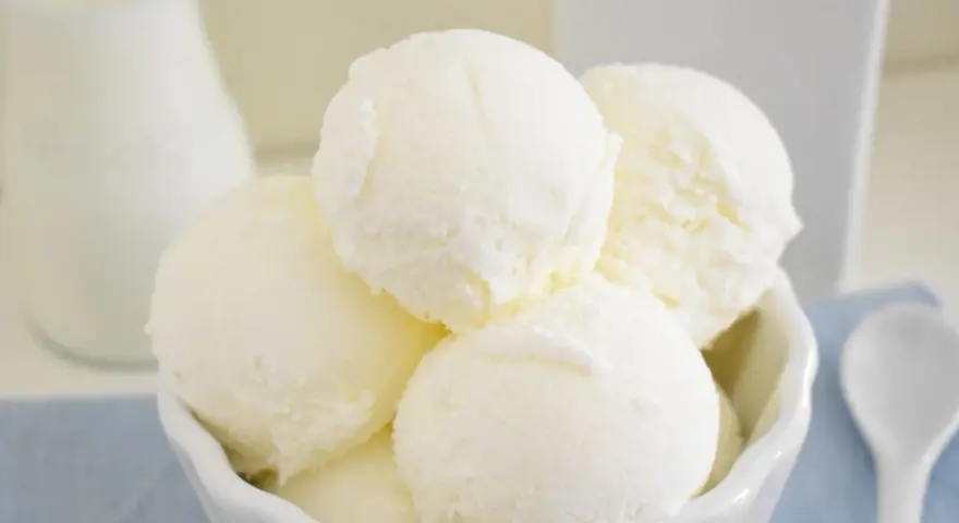 Coppa di gelato cremoso, risultato di una perfetta ricetta gelato con gelatiera. Latte fresco e cucchiaino bianco.