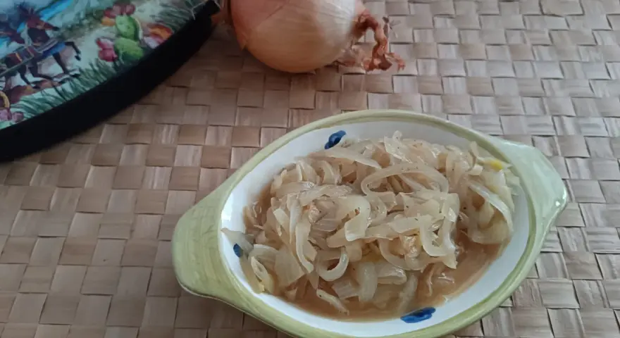 Ciotola con cipolle in agrodolce, accanto una cipolla intera e un piatto decorato.