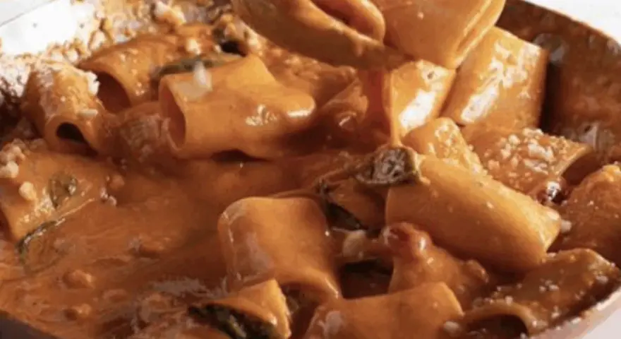 Un primo piatto cremoso e invitante: paccheri alla Vittorio, conditi con una ricca salsa arancione e guarniti con parmigiano.