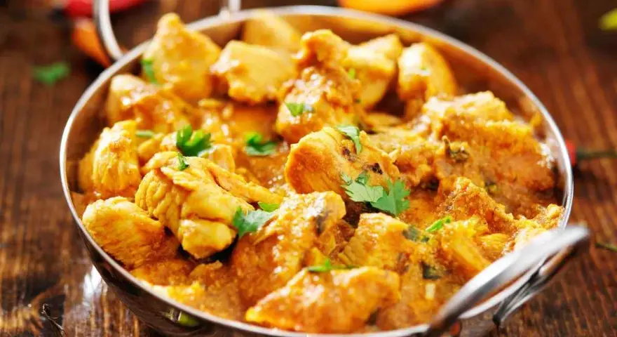 Bocconcini di pollo al curry, un piatto speziato e profumato, servito in una ciotola metallica su un tavolo di legno.