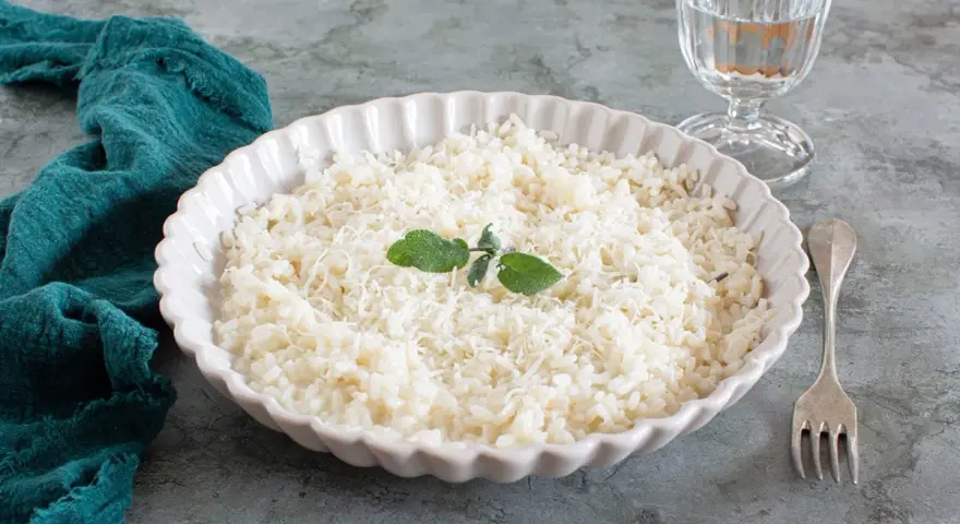 Piatto di riso in cagnone, cremoso e invitante, guarnito con foglie di salvia e parmigiano grattugiato.