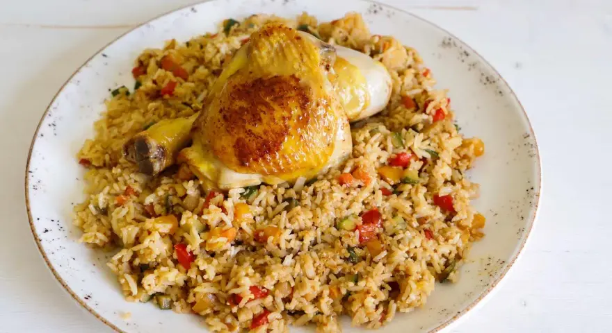 Fusi di pollo in padella serviti su un letto di riso saltato con verdure colorate.