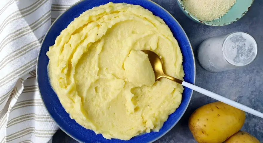 Un piatto invitante di puro di patate cremoso, pronto per essere gustato. Accanto, patate fresche, sale e formaggio grattugiato.