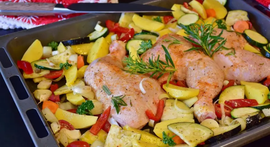 Sovracosce di pollo al forno con patate, zucchine, peperoni e rosmarino, pronte per essere infornate.