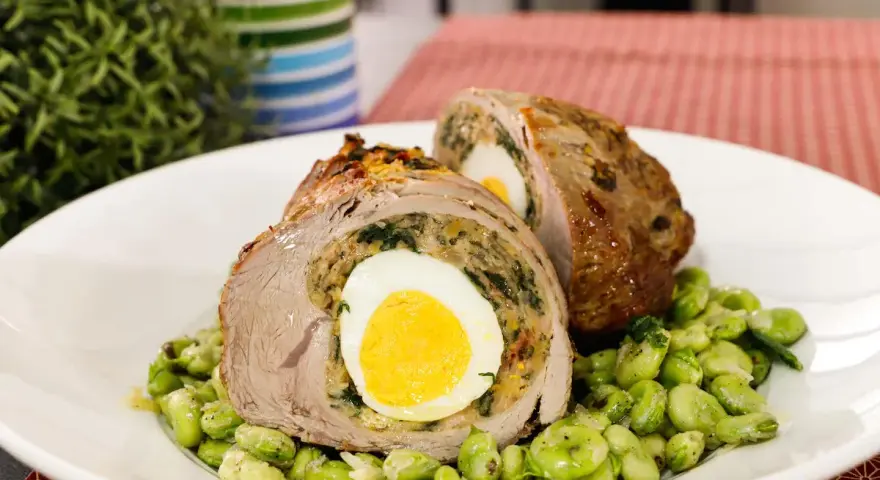 Fettina di carne ripiena con uovo sodo e spinaci, servita su un letto di fave.