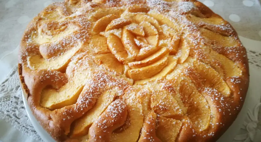 Deliziosa torta di mele senza glutine, con mele disposte a rosa al centro e spolverata di zucchero a velo.