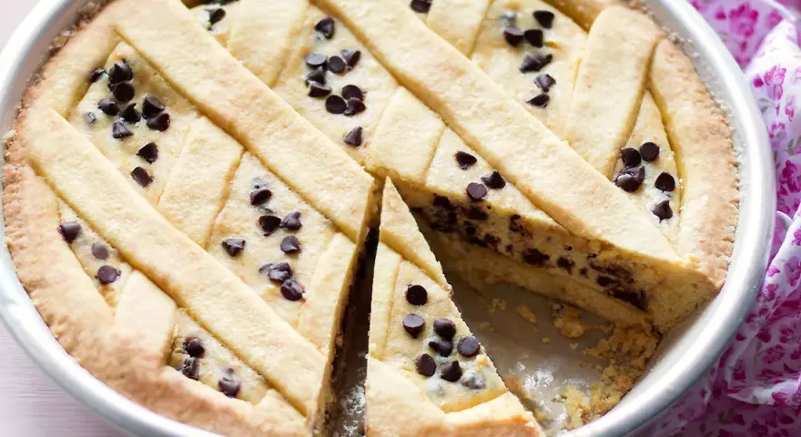 Una deliziosa crostata di ricotta con gocce di cioccolato, con una fetta tagliata per mostrare il ripieno cremoso.