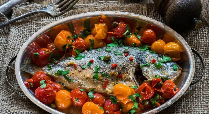 Orata all'acqua pazza, un piatto saporito con pomodorini, capperi e prezzemolo, pronto per essere gustato.