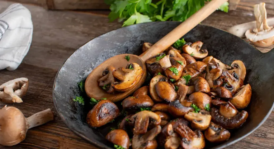 Funghi in padella dorati e saporiti, guarniti con prezzemolo fresco, pronti per essere gustati.