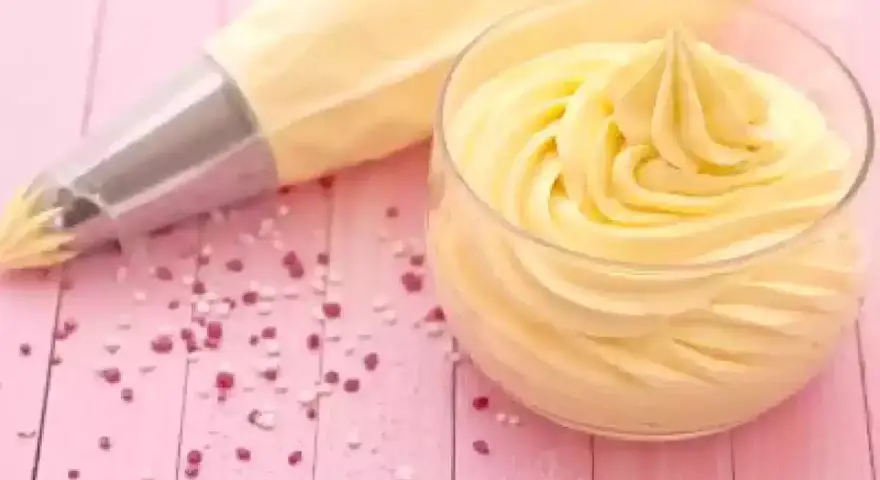Sac à poche con crema al burro pronta per decorare, accanto a un bicchiere colmo della stessa soffice crema.