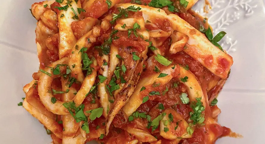 Un piatto invitante di calamari in umido, conditi con una ricca salsa al pomodoro e prezzemolo fresco tritato.