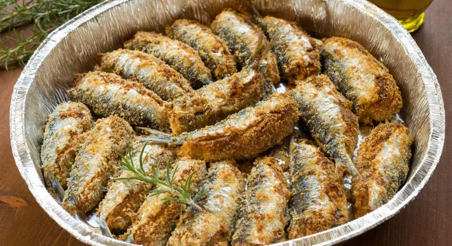 Sardine al forno dorate e croccanti, disposte in una teglia d'alluminio con rametti di rosmarino.