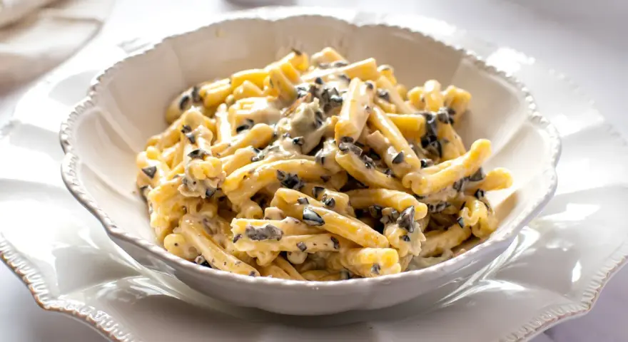 Un piatto di pasta alla cenere cremosa, con pezzetti scuri di olive, servita in una ciotola bianca decorata.
