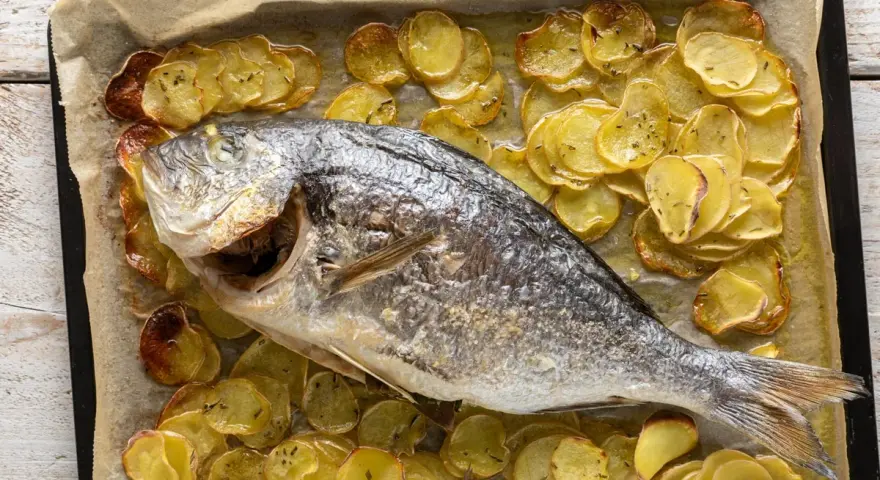 Orata al forno dorata e succulenta, adagiata su un letto di patate croccanti e aromatiche.