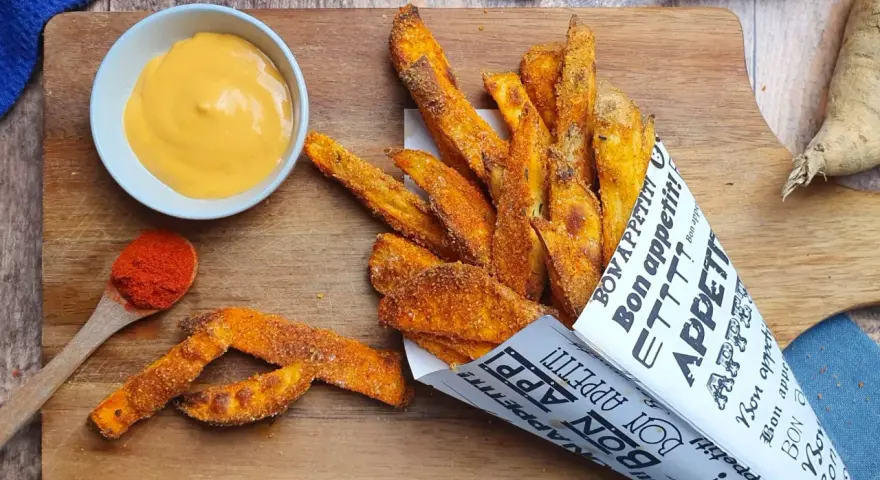 Patate dolci al forno croccanti, servite in un cono di carta con una salsa cremosa e paprika.