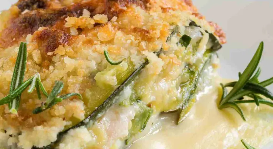 Una fetta di parmigiana di zucchine bianca senza besciamella, dorata e croccante, con rosmarino fresco.