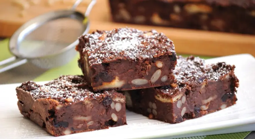 Fette di torta di pane al cioccolato, ricche di frutta secca e noci, spolverate di zucchero a velo.