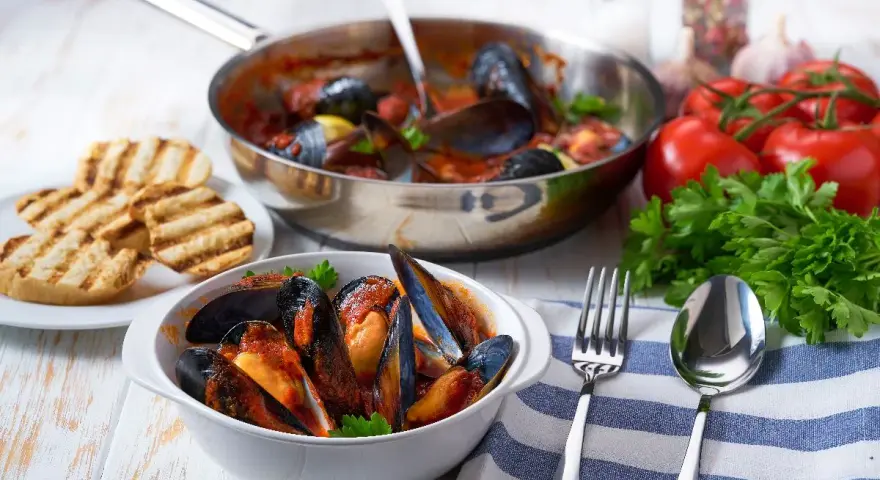Cozze alla tarantina fumanti in una ciotola bianca, accompagnate da pane grigliato e ingredienti freschi.