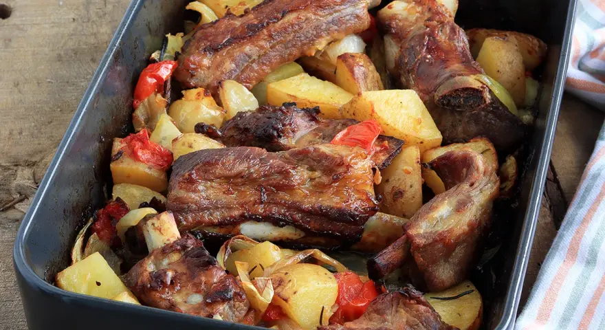 Succulente costine al forno con patate, peperoni e cipolle in una teglia.