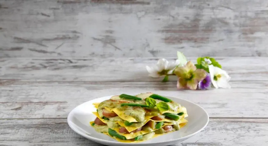 Lasagne al pesto con fagiolini e patate, un piatto colorato e gustoso su un tavolo di legno.