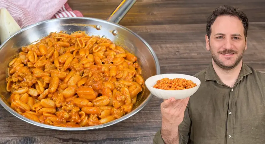 Un uomo sorride mostrando una ciotola di gnocchetti alla campidanese, accanto a una padella piena dello stesso piatto.