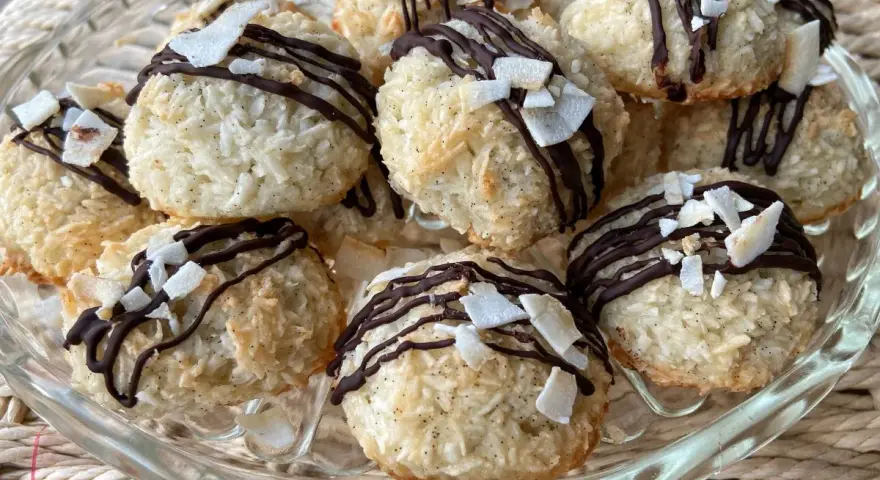 Deliziosi dolcetti al cocco, ricoperti da cioccolato fondente e scaglie di cocco croccante, su un piatto di vetro.
