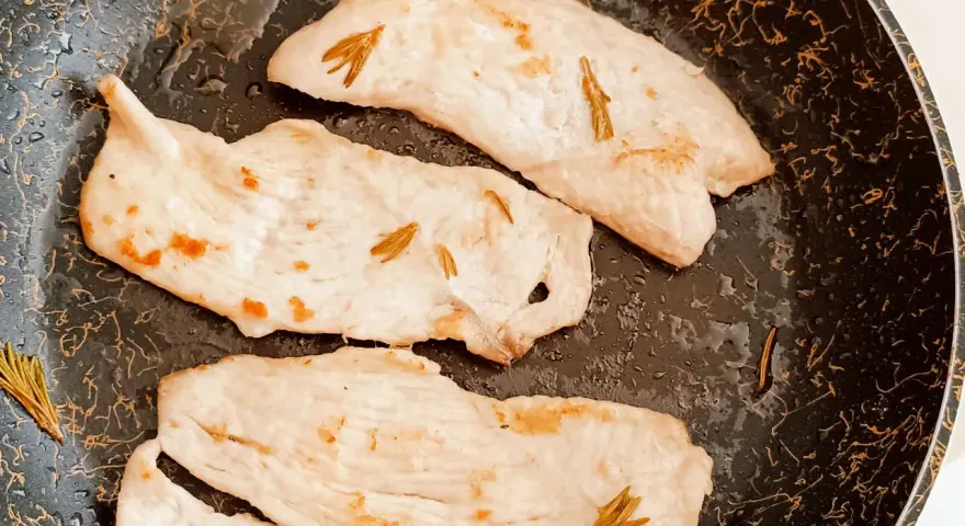 Tre fette di tacchino in padella, morbido e profumato al rosmarino, pronte per essere gustate.