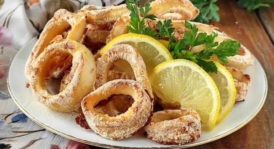 Anelli di calamari al forno dorati e croccanti, guarniti con spicchi di limone fresco e prezzemolo.
