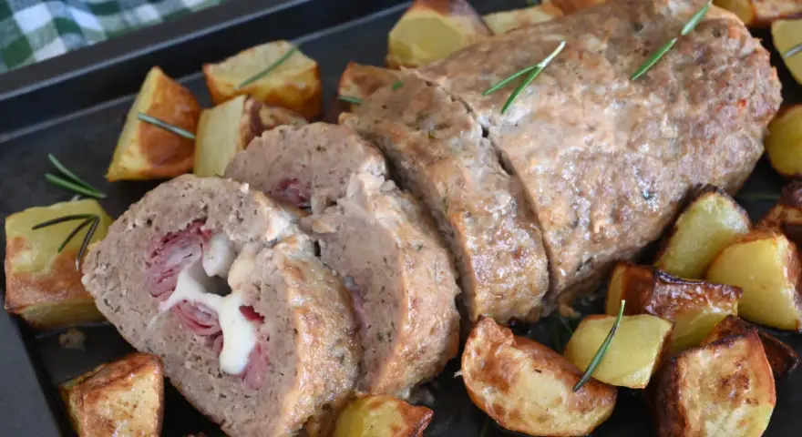 Polpettone al forno ripieno di prosciutto e formaggio filante, servito con patate arrosto e rosmarino.