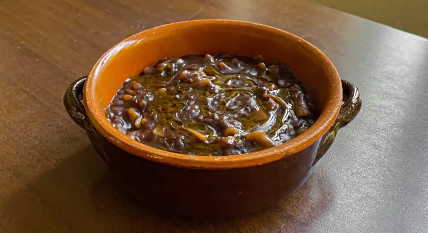 Un gustoso piatto di pasta e lenticchie, condito con olio d'oliva, servito in una ciotola di terracotta su un tavolo di legno.