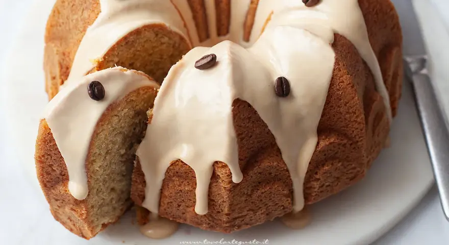 Torta al caffè soffice e profumata, ricoperta da una glassa chiara e decorata con chicchi di caffè. Una fetta è stata tagliata, rivelando l'interno morbido.