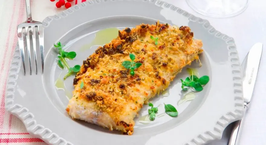 Delizioso merluzzo impanato al forno, dorato e croccante, guarnito con erbe fresche e servito su un piatto grigio.
