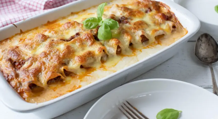 Cannelloni ripieni di carne macinata e mozzarella, cotti al forno e gratinati, con una foglia di basilico fresco.