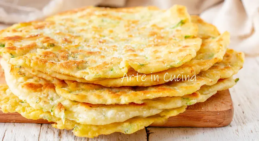 Una pila di schiacciate di zucchine dorate e soffici, cosparse di parmigiano, pronte per essere gustate.