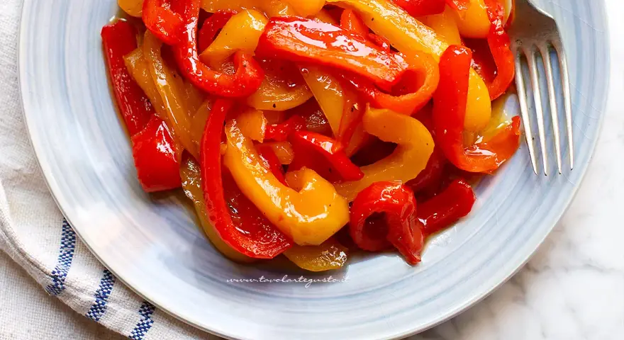 Piatto di peperoni in agrodolce, rossi e gialli, conditi con olio e spezie, pronti per essere gustati.