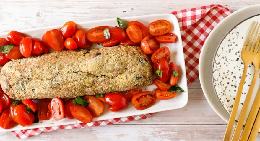 Polpettone di melanzane dorato e croccante, circondato da pomodorini freschi e basilico, pronto per essere gustato.