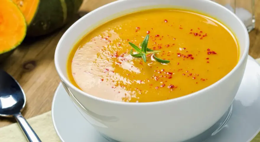 Una cremosa vellutata di zucca, guarnita con rosmarino e paprika, pronta per essere gustata.