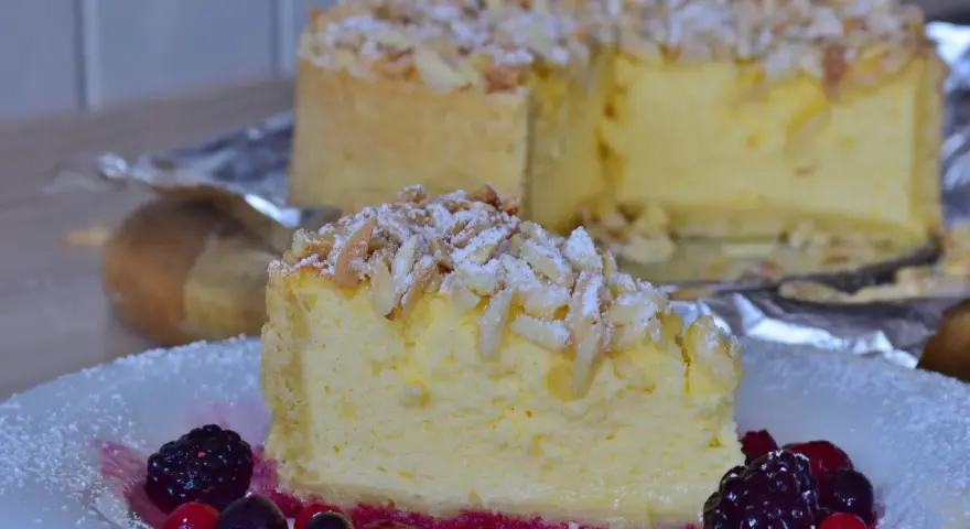 Una fetta di torta di riso cremosa, guarnita con mandorle a lamelle e frutti di bosco, su un piatto bianco.