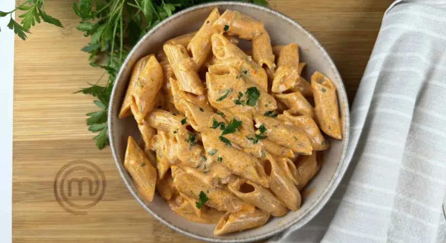 Penne alla vodka cremose e invitanti, guarnite con prezzemolo fresco, su un tagliere di legno con il logo di MasterChef.