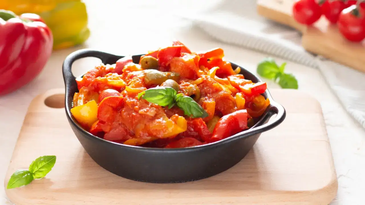 Un piatto fumante di peperonata ricetta della nonna, con peperoni rossi e gialli, olive e basilico fresco.