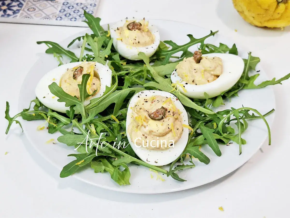 Uova sode ripiene, un antipasto sfizioso su un letto di rucola, guarnite con scorza di limone e pepe.