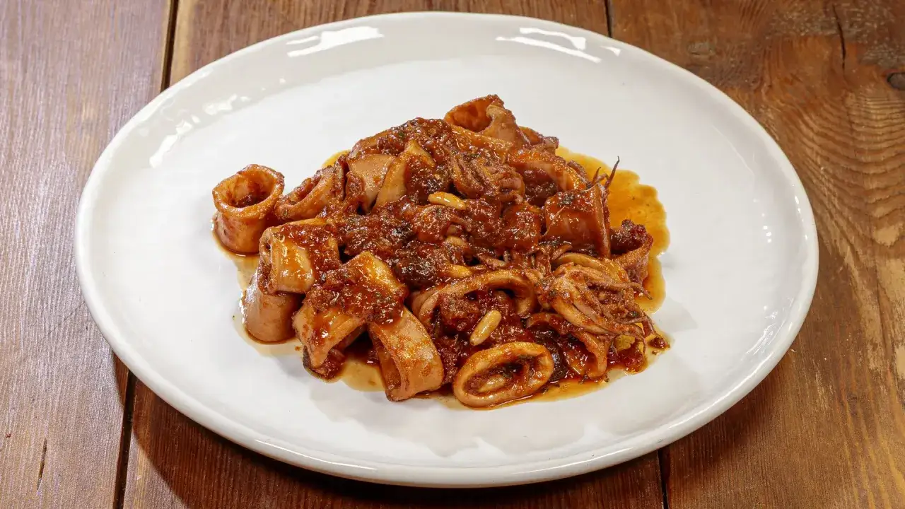 Un piatto invitante di calamari in umido, con anelli e tentacoli immersi in un sugo ricco e saporito, guarnito con pinoli.