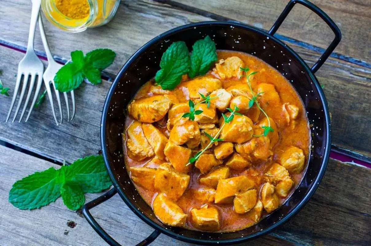 Bocconcini di pollo al curry cremosi e profumati, guarniti con menta fresca e timo, pronti per essere gustati.