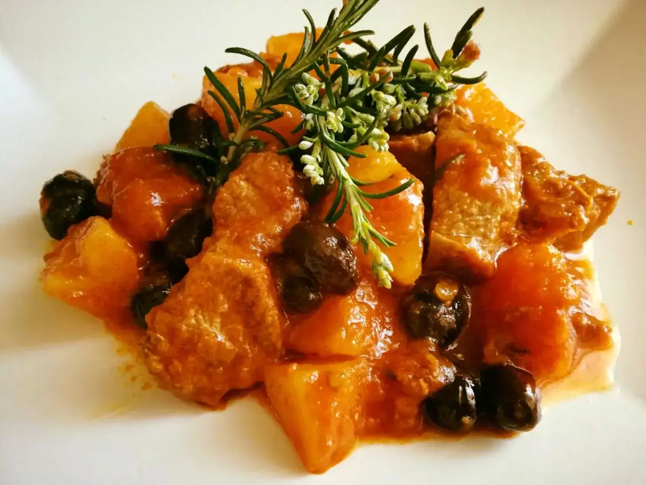 Un saporito spezzatino di manzo con patate e olive nere, guarnito con rosmarino fresco.