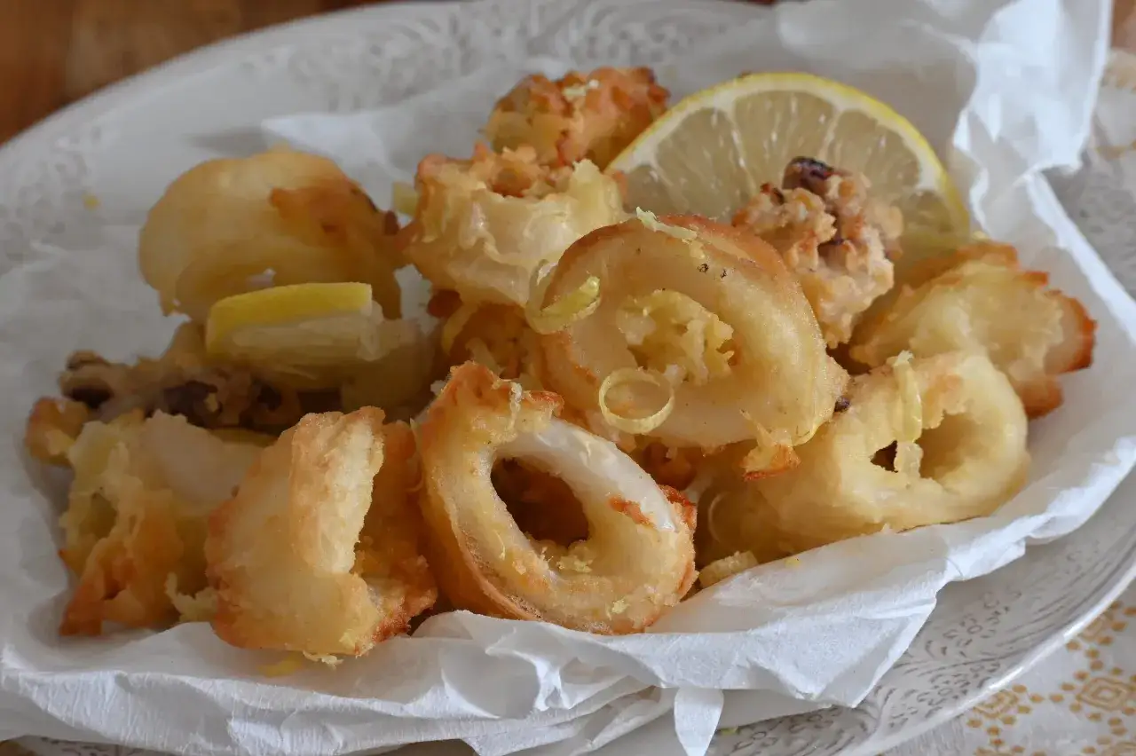 Un piatto di frittura di calamari dorata e croccante, guarnita con spicchi di limone e scorzette.